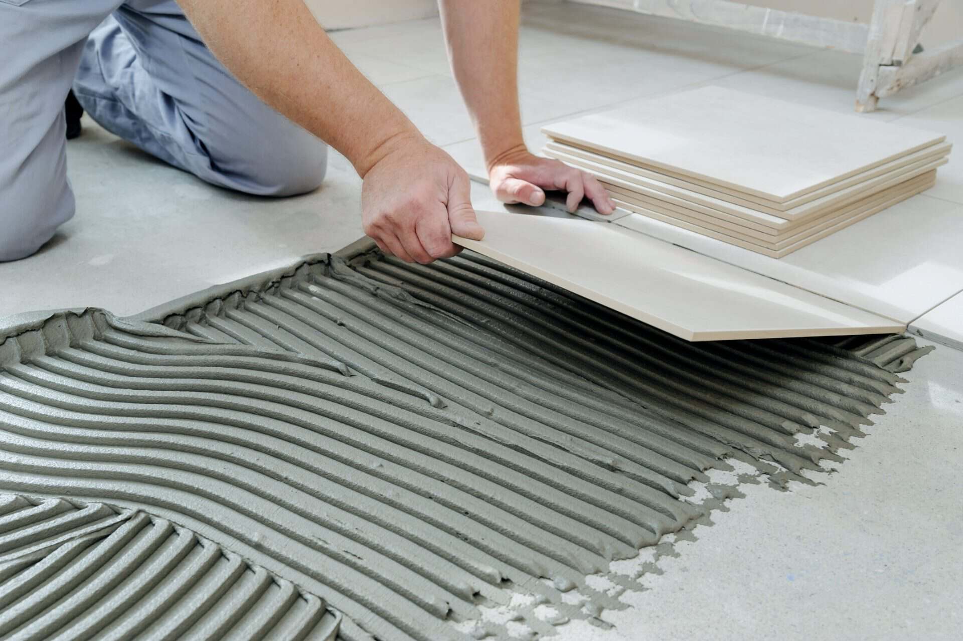 The hands of the tiler are laying the ceramic tile on the floor.