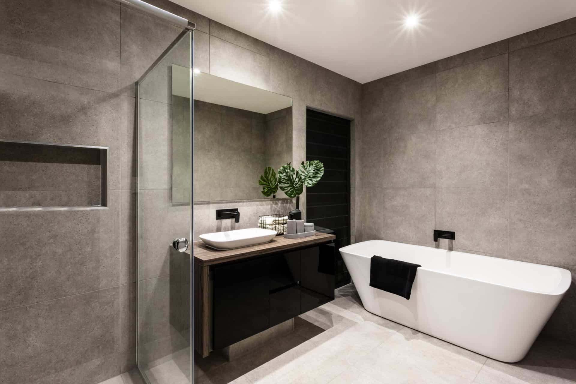 Modern bathroom with a shower area and bath tub including a wall mirror beside a fancy plant near a tap and sink over the wooden counter and dark cupboard